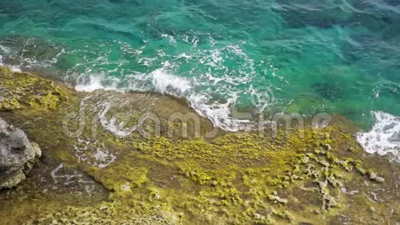晴天鸟瞰绿松石海在缓慢运动中溅到岩石上的海浪的俯视图视频的预览图