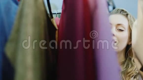 年轻的白种人女人看着衣服挂在衣架上妇女服装店购物视频的预览图