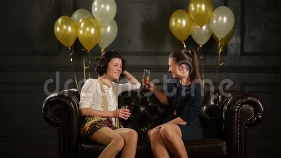 两位美丽的女士在棕色沙发上坐着香槟酒杯在聚会上谈论一些有趣的事情视频的预览图