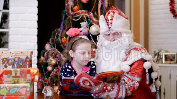 漂亮漂亮的金发女郎头发上有一个粉红色的蝴蝶结穿着一件漂亮的裙子正在和圣诞老人的父亲一起看书视频的预览图