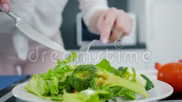 手拿刀叉在厨房里混合新鲜的有机绿色沙拉生菜和西兰花和黄瓜视频的预览图