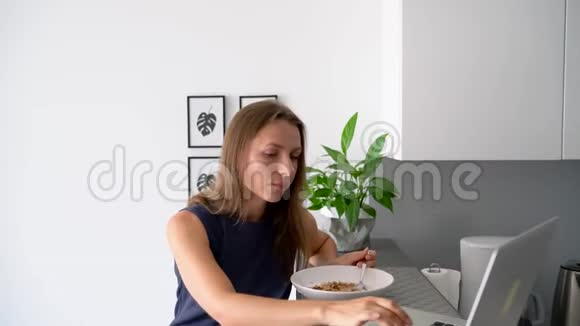 有魅力的女人一边吃早餐一边用笔记本电脑视频的预览图