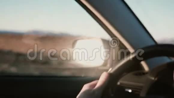 在美丽的日落中在乡村沙漠道路上的车内观看近景男性手在车轮上视频的预览图