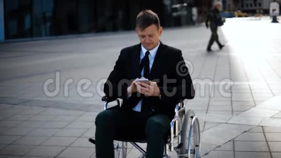 坐在轮椅上的年轻商人正在玩或使用他的智能手机视频的预览图