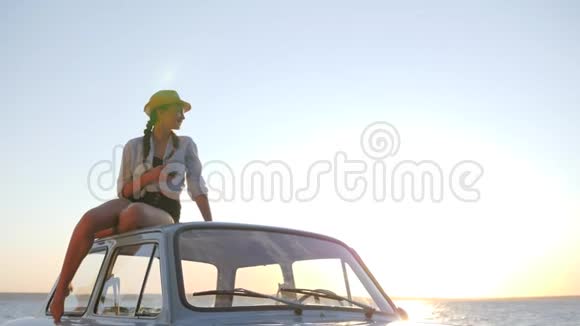 女孩在河边的旧机器的屋顶上手里拿着小玩意夕阳的背光上从女性到老式汽车视频的预览图