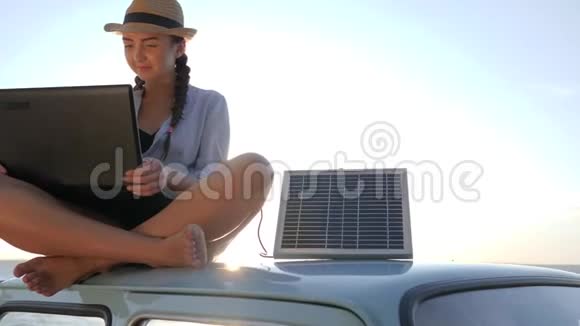 旅行年轻女子坐在汽车车顶笔记本和太阳能电池板背景海洋海岸背光视频的预览图