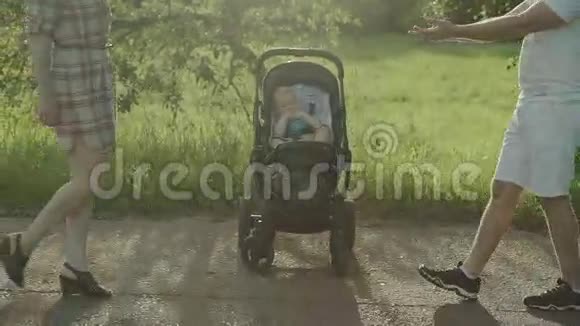 快乐的年轻父母带着婴儿坐在公园的马车里家庭游乐场夏季晴天慢动作4k视频的预览图