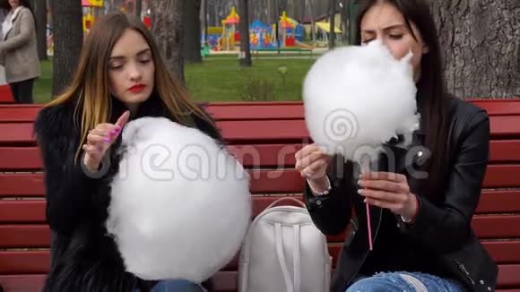 可爱的女孩坐在长凳上吃棉花糖视频的预览图