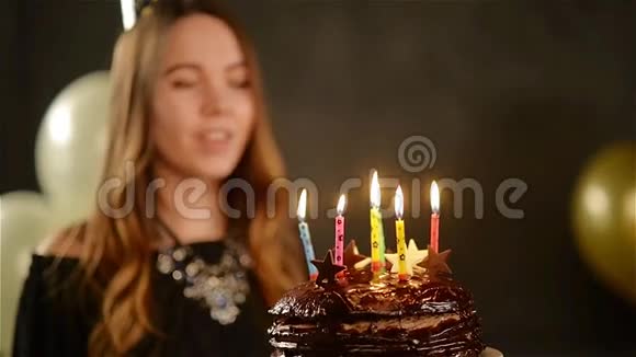 留着长发的可爱少女在黑色背景下用金色和白色的巧克力蛋糕吹着蜡烛视频的预览图