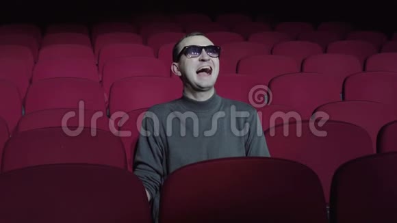 一个单身男人坐在黑色电影院里舒适的红椅子上笑视频的预览图