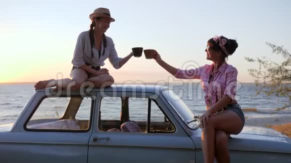 在日落的时候女孩们手里拿着杯子在海边开车在日落的时候朋友们的茶会在海岸上机器视频的预览图
