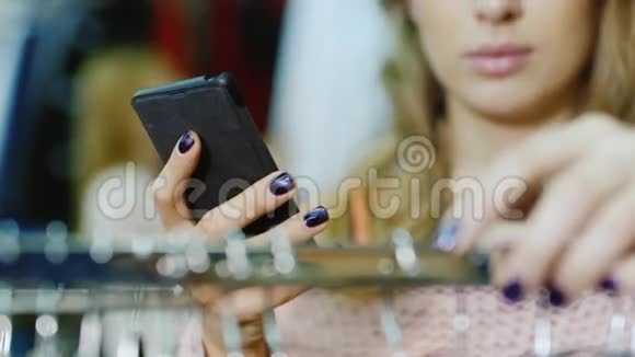 女人在商店里选择一件衣服看智能手机照片文件夹在一个大的可见的手和电话的框架内视频的预览图