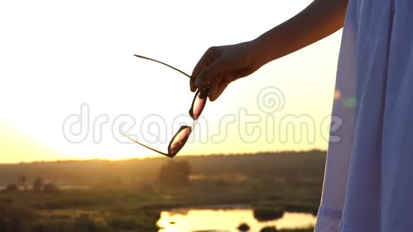 一个年轻的苗条女人站在斯隆莫的夕阳下手里拿着太阳镜视频的预览图