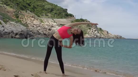 健康运动的女人在靠近海边的海滩上跑步之前锻炼和伸展身体以热身女性在一边视频的预览图