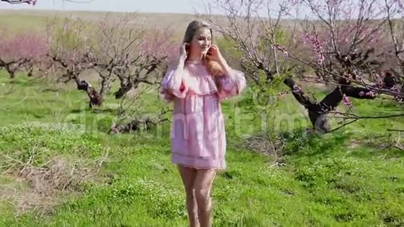 一位身着粉色礼服的金发女子在一个盛开的花园里挂着桃树视频的预览图