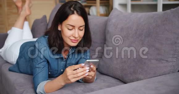 微笑的年轻女士用智能手机拿着小玩意在家里触摸屏幕视频的预览图