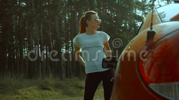 可爱的年轻女士戴着太阳镜戴着红唇在树林里摆着一辆红色的车视频的预览图
