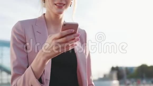 漂亮的金发女商人穿着粉红色时髦的服装经过机场商务中心使用她的手机和视频的预览图