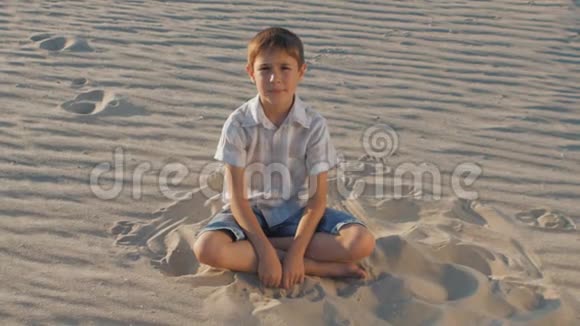 夏天穿着白色衬衫的可爱男孩坐在沙滩上的肖像视频的预览图