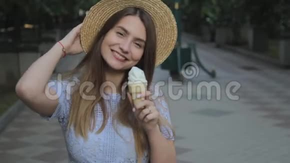 一个戴着帽子和蓝色夏装的年轻女孩舔着美味的香草冰淇淋视频的预览图