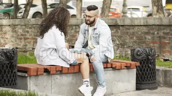 恋爱中的情侣坐在公园的长凳上互相看着视频的预览图