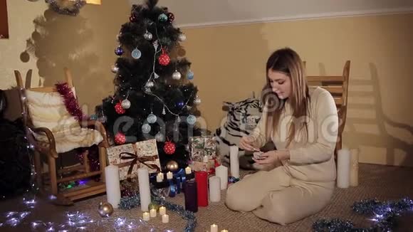 美丽的少女坐在圣诞树旁的地板上吹蜡烛视频的预览图