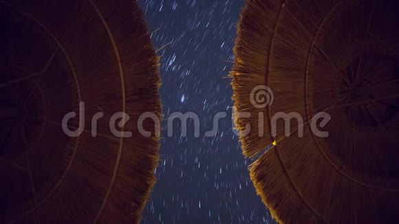 星星小径在深蓝色的天空中追踪背景风景在前景上有对称的海滩伞视频的预览图