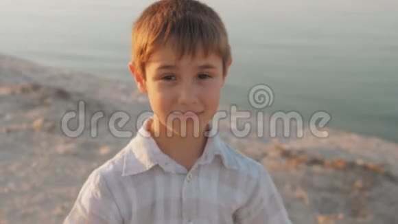 一个10岁的男孩在日落的背景下在海边的夏日海滩上微笑的肖像视频的预览图