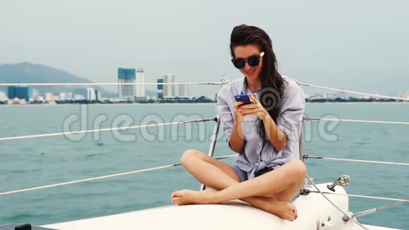 年轻女子坐在游艇上用智能手机微笑视频的预览图