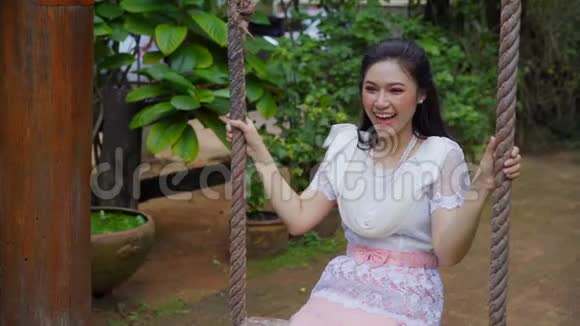 穿着泰国传统服装的快乐年轻女子在木制秋千上放松视频的预览图