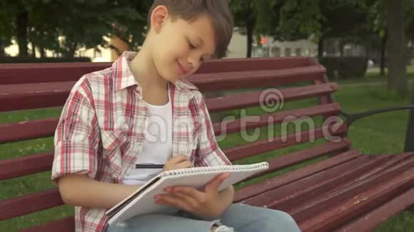 小男孩在长凳上的练习本上记笔记视频的预览图