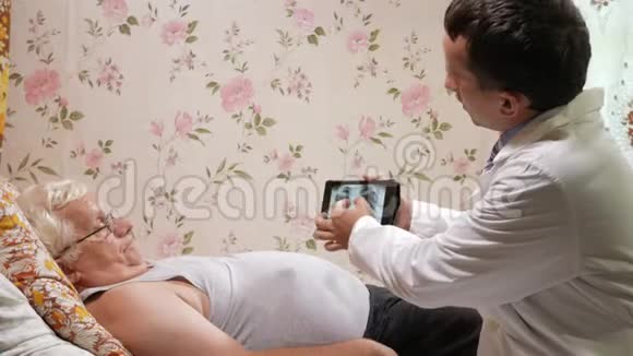 一位男医生在家看望病人它显示了平板电脑上X射线的结果那个人躺在床上视频的预览图