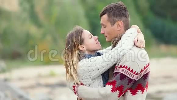 一对年轻漂亮的夫妇穿着针织毛衣在海边的悬崖上逗弄拥抱和亲吻男人在他的女朋友身上挥挥手视频的预览图