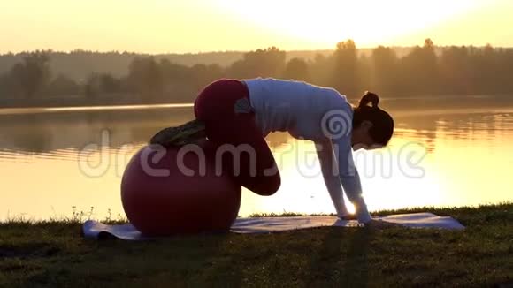 苗条的女人在日落时用健身球弯曲她的腿视频的预览图