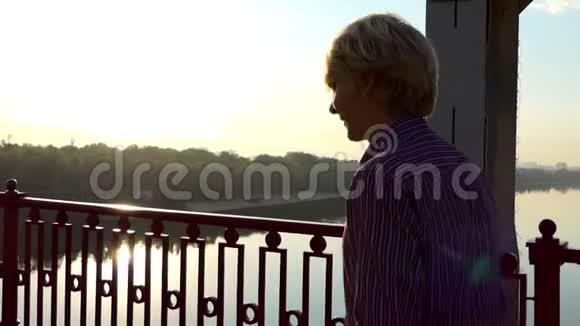 夏天在斯隆莫的一座河桥上年轻的金发男子在灿烂的夕阳下漫步视频的预览图