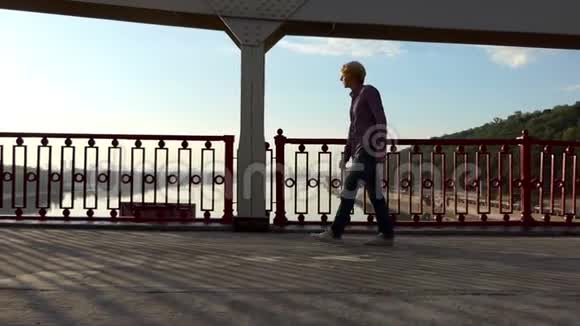 年轻人在缓慢运动的河桥上漫步享受灿烂的日落视频的预览图