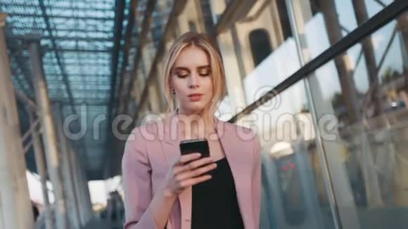 自信的性感金发女孩走在商务中心用她的手机时尚的外观优雅的白色视频的预览图