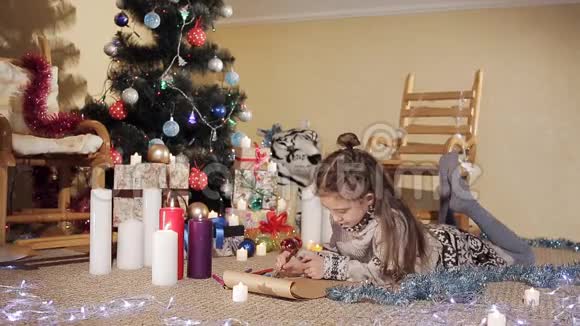 可爱的小女孩躺在圣诞树附近的地板上画了一张贺卡视频的预览图