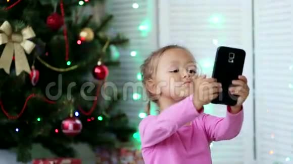 小可爱的女孩在背景上用圣诞树自拍视频的预览图