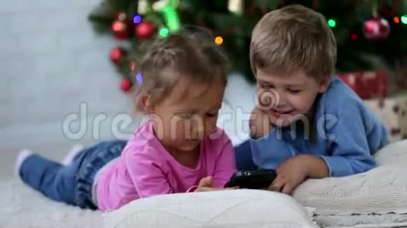 可爱的兄弟姐妹在圣诞树附近的手机里怀着滑稽的表情视频的预览图