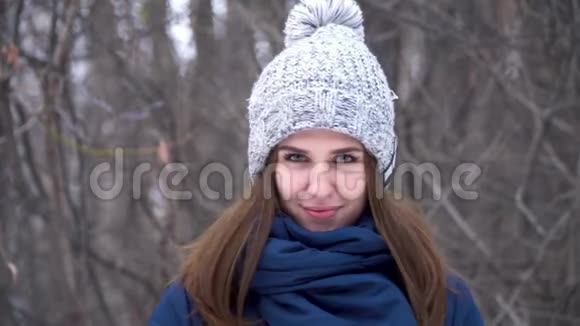 穿着冬装帽子和围巾的美丽年轻微笑的白种人女子的特写肖像布鲁纳女孩雪木视频的预览图