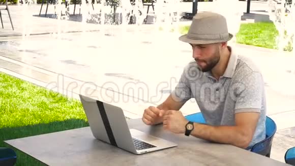英俊的男性有趣地看足球比赛与笔记本电脑附近的喷泉视频的预览图