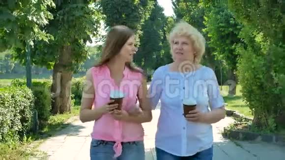 幸福的老妇人和年轻女子走公园小巷喝咖啡成年母亲和女儿在公园散步视频的预览图
