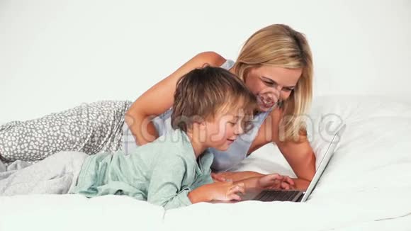 4岁的男孩和妈妈躺在床上玩笔记本视频的预览图
