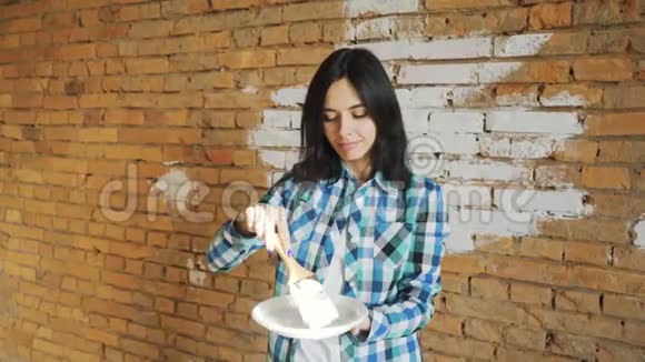 女孩刷白砖墙海丝特女孩在家里粉刷墙壁手里拿着一把带油漆的刷子视频的预览图