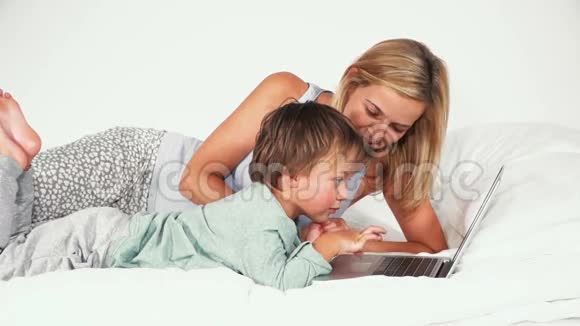 4岁的男孩和妈妈躺在床上玩笔记本视频的预览图