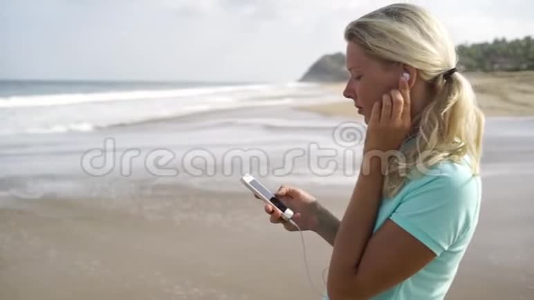 在沙滩上听智能手机音乐的女人视频的预览图