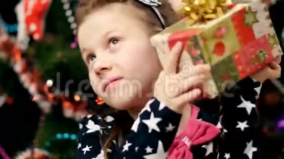 可爱的金发女孩她的头发上有一个粉红色的蝴蝶结穿着一件漂亮的优雅连衣裙好奇地看着她的圣诞礼物视频的预览图