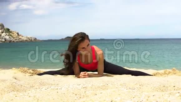 年轻的运动女性做伸展运动坐在靠近大海的海滩上的小树枝上视频的预览图