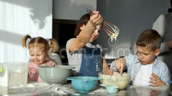 厨房里三个快乐的孩子把面团揉成馅饼妈妈帮他们筛面粉家庭烹饪花冠视频的预览图